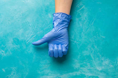 Covid-19 prevention. Medical support. Hand in protective gloves showing thumb up on textured blue....