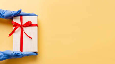 Birthday surprise. Pandemic hygiene. Hands in protective gloves holding present box red ribbon....