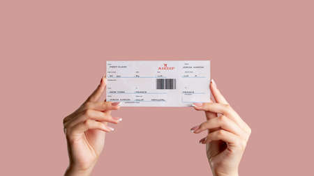 Female passenger hands holding first class ticket isolated on pale pink copy space.