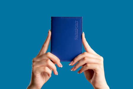 Passport service. Visa center. Female hands holding national id book in blue cover isolated on bright copy space background. Legal document. Global immigration.の写真素材