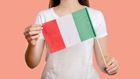 Italy flag. European tour. Woman holding official national symbol tricolor with three vertical green white red stripes isolated on blur coral pink background. National culture.の写真素材