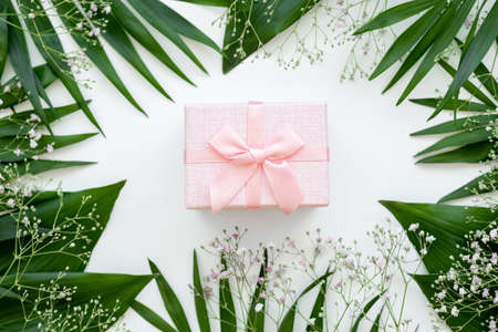 Holiday present. Floral composition. Pink gift box with ribbon bow in green leaf frame isolated on white. Natural arrangement. Festive background.の写真素材
