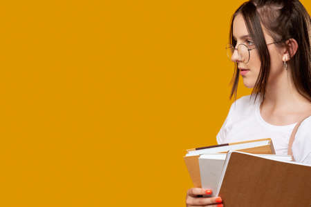 Smart student. High school. Young woman in glasses holding many notebooks. Isolated on orange copy...
