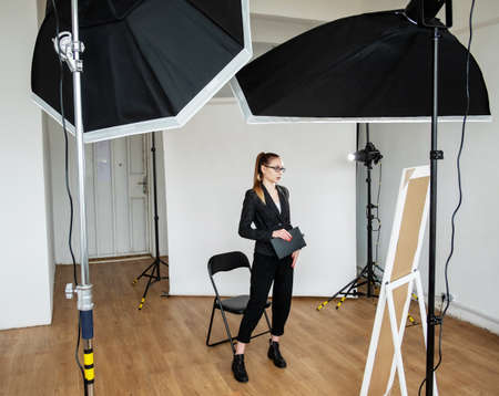 Photo shoot backstage. Professional photography. Female producer standing in modern studio with light equipment white backdrop. Master class. Creative crew.の写真素材
