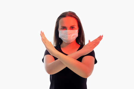 Stop sign. Forbidden gesture. Worried woman in protective mask red glow crossing hands looking at camera isolated on white copy space. Stay home. Quarantine measures. Pandemic restriction. New normalの写真素材