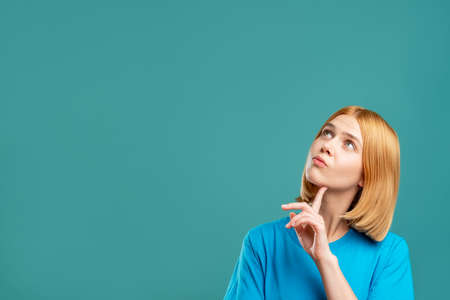 Curious woman. Motivation background. Portrait of pensive blonde lady in blue t-shirt looking at empty space for information isolated on teal. Dream opportunity.の写真素材