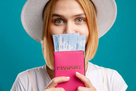 Summer trip. Vacation tour. Happy woman in white holding foreign passport with tickets. Looking at camera isolated on blue. Travel agency. Visa officeの写真素材
