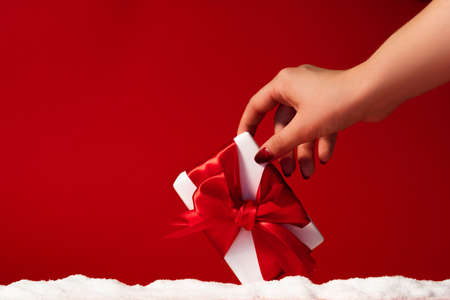 Christmas surprise. Winter holidays present. Female hand taking wrapped white gift box with ribbon...