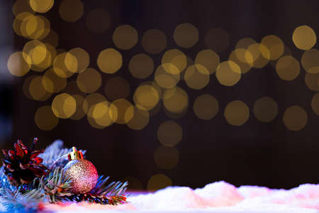 Christmas holiday. Festive decoration. New Year. Pine branch with cone and tree ball on snowy decor composition in shimmering bokeh lights background copy space.の写真素材
