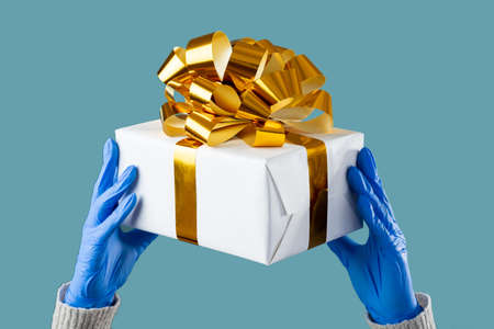 Holiday gift. Christmas new year 2021. Female hands in medicine gloves holding present box with...