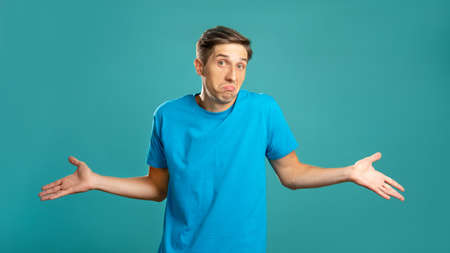 Puzzled male portrait. Careless gesture. Helpless emotion. So what. Doubtful expressive man shrugging looking at camera isolated on blue.の写真素材