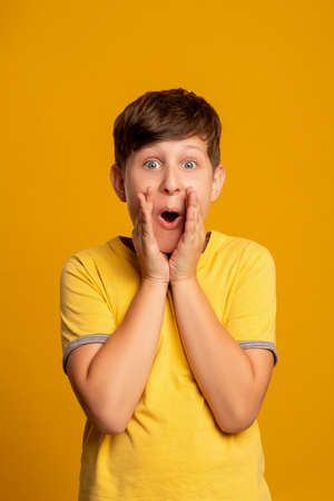 Excited child. Unbelievable success. Victory celebration. Dream opportunity. Portrait of surprised amazed young boy with open mouth supporting isolated on orange background.の写真素材
