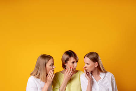 Female friendship. Gossip rumor. Women lifestyle. Portrait of three worried disturbed ladies whispering discussing sharing secret isolated on orange copy space background.の写真素材