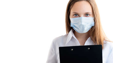 Sales representative. Covid-19 measures. Office woman. Young lady in protective mask holding black clipboard looking at camera isolated on white copy space. Advertising backgroundの写真素材
