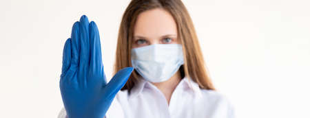 Stop gesture. Quarantine measures. Closed office. Covid-19 restriction. Woman in protective mask gloves showing forbidden hand isolated on white copy space.の写真素材