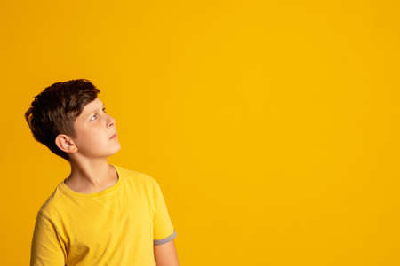 Hard choice. Curious kid. Knowledge discovery. Tough decision. Doubtful pensive young boy looking at copy space considering option isolated on orange commercial background.の写真素材