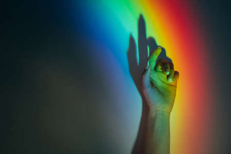 LGBT pride. Diversity freedom. Gender rights. Trance recreation. Graceful female hand in blur rainbow lights. Iridescent blue red green yellow color gradient glow on dark copy space background.の写真素材
