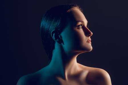 Profile silhouette of confident woman with bare shoulders in blue glow isolated on dark copy space background.の写真素材