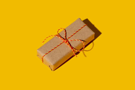 Handmade present. Gift delivery. Care package. Holiday surprise. Vintage rustic beige simple paper box with orange twine bow isolated on bright yellow empty space background.の写真素材