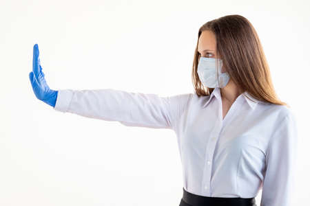 Stop gesture. Keep distance. Quarantine measures. Office work. Woman in protective mask gloves showing forbidden hand isolated on white copy space side view.の写真素材