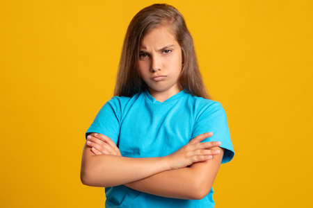 Offended child. Disobedience bullying. Kid punishment. Failure blame. Portrait of upset young girl in blue t-shirt with folded arms looking at camera isolated on orange copy space background.の写真素材