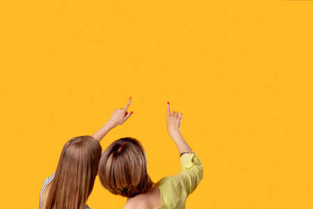 Information announcement. Inspiration motivation. Solution discovery. Two curious women reading virtual invisible text pointing up isolated on orange copy space commercial background.の写真素材