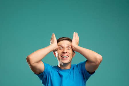 Unbelievable success. Great achievement. Euphoric emotion. Got it. Expected result. Invisible message. Excited young man holding head looking up copy space isolated on blue.の写真素材