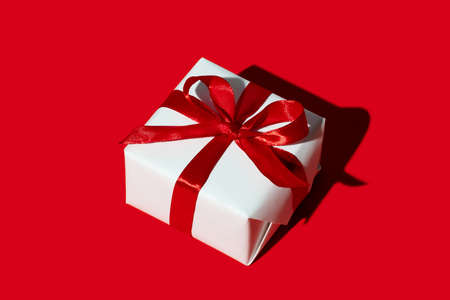 Christmas gift. Holiday surprise. Care package. New Year decoration. Present wrapped in white box with ribbon bow isolated on red copy space background.の写真素材