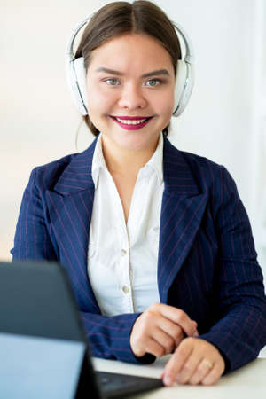Online education. Zoom webinar. Elearning coaching. Virtual class. Cheerful confident business woman in white headphones with laptop on light background.の写真素材