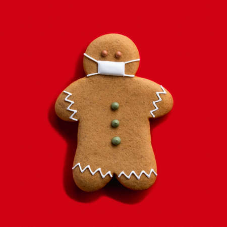 Quarantine celebration. Covid-19 winter holidays. Brown gingerbread man in protective face mask...