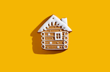 Christmas biscuit. Festive bakery food. Winter holidays ornament. Beige gingerbread house cookie with white snow icing creative decoration isolated on yellow copy space background.の写真素材