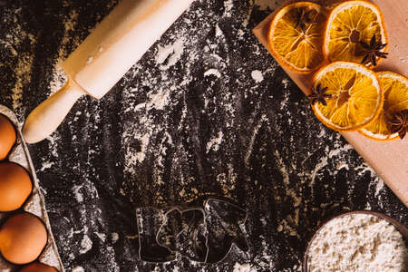 Christmas food background. Festive culinary. Homemade bakery. Meal powdered black desk with eggs rolling pin dried orange spices copy space.の写真素材