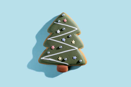 Christmas tree illustration. Festive decorated bakery. Traditional cookies art. Gingerbread green icing figure biscuit white ornament isolated on blue pastel background.の写真素材