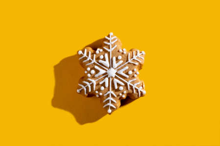Xmas cookie. Winter holidays ornament. New Year celebration symbol. Beige homemade gingerbread snowflake with white icing isolated on yellow empty space background.の写真素材