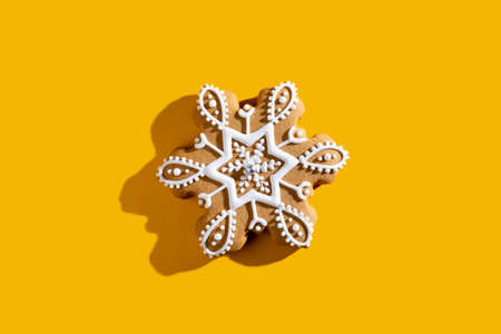 Christmas biscuit. Winter holidays food art. Festive adornment. Beige homemade gingerbread snowflake shape cookie with white icing isolated on orange copy space background.の写真素材