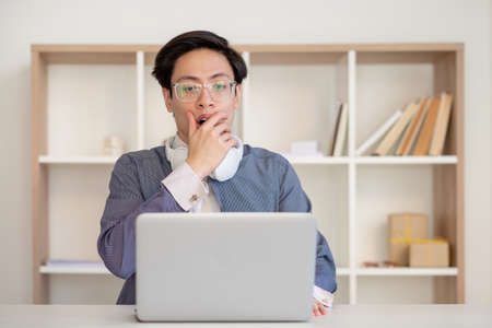 Professional mistake. Work problem. Project failure. Virtual meeting. Scared asian male employee in glasses looking at laptop at light workspace.の写真素材