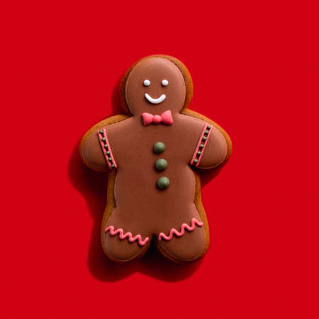 Homemade cookie. Bakery food art. Festive sweet ornament. Brown happy smiling gingerbread man shape biscuit with chocolate icing decor isolated on red background.の写真素材