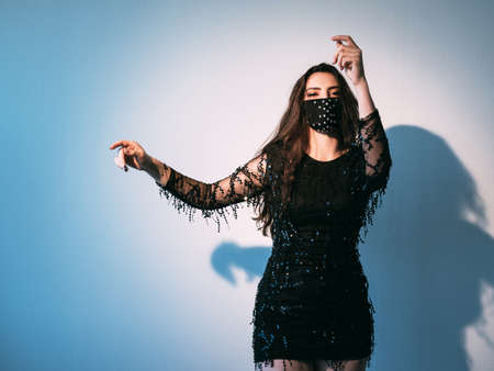 Pandemic party. Night club look. Fashion trend 2021. Brunette woman in black handmade face mask...