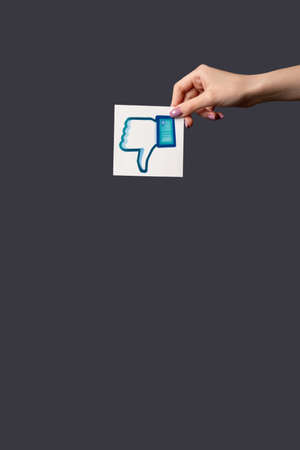 Kharkiv, Ukraine - June 05, 2020: Dislike icon. Social media. Online disagreement. Woman hand holding thumb down sign isolated on dark purple empty space background.のeditorial素材