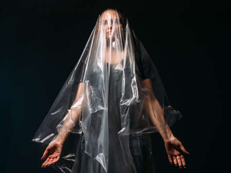 Art portrait. Depressed woman. Domestic violence. Female rights. Art portrait of enslaved lady covered with head in clear cellophane plastic film bag isolated on black copy space background.の写真素材
