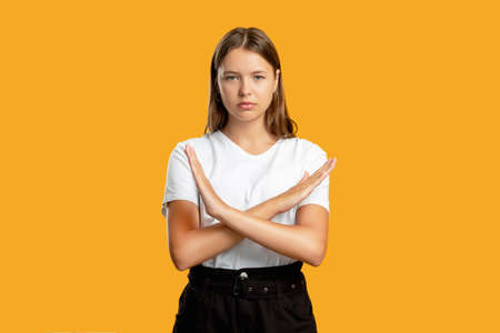 Nope gesture. Female strike. Refusal sign. Disagreement opposition. Portrait of confident teen girl in white showing X restriction with crossed hands isolated on orange copy space background.の写真素材