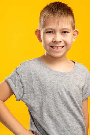 Happy kid portrait. Fun childhood. Positive attitude. Amused satisfied young boy in gray t-shirt smiling looking at camera isolated on yellow background.の写真素材