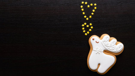 Valentine Day. Greeting card. Festive background. Creative holiday congratulation. Cute white gingerbread deer singing with gold star hearts on black wooden texture copy space.の写真素材