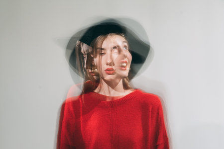 Defocused female portrait. Personality disorder. Art fashion. Tranquility thoughts. Silhouette woman in red sweater black hat sad serious happy isolated on neutral double exposure blur.の写真素材