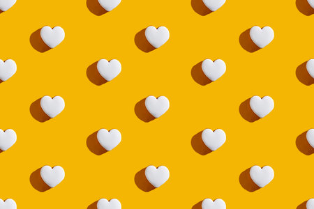Heart pattern. Yellow seamless background. Valentine Day. Romantic greeting card. White love symbol decorative festive minimalist arrangement isolated on bright orange.の写真素材