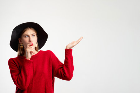 Trend look. Make choice. Personal style. Sale discount. Consider offer. Doubtful hipster woman in red sweater black hat pointing copy space thinking isolated on white. Advertising background.の写真素材