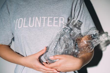 Plastic recycling. Zero waste. Social work. Environmental protection. Unrecognizable volunteer woman in t-shirt holding used creased bottles on gray background.の写真素材