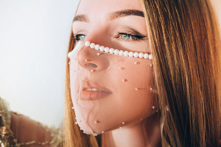 Pandemic fashion. Oriental beauty. Wedding look. Inspired woman in designer sheer pearl beads decorated face mask isolated on light background.の写真素材