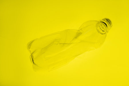 Plastic pollution. Waste recycling. Environmental protection. Used creased empty bottle floating on vibrant yellow copy space art background.の写真素材