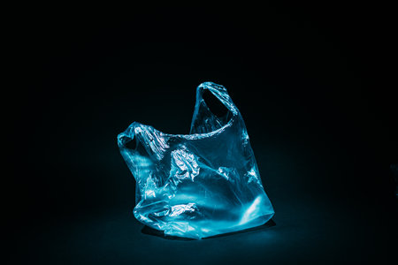 Plastic pollution. Waste contamination. Ecology problem. Blue empty used cellophane bag floating underwater in abstract ocean abyss isolated on dark copy space background.の写真素材